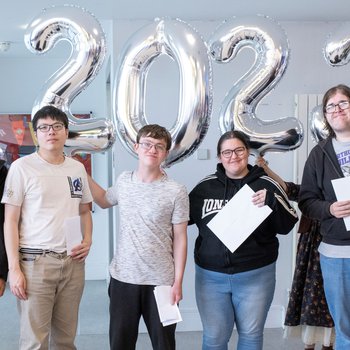 A group of learners stand in front of balloons spelling 2023