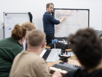A man wearing a blue jumper teaching 3 young people using a whiteboard.