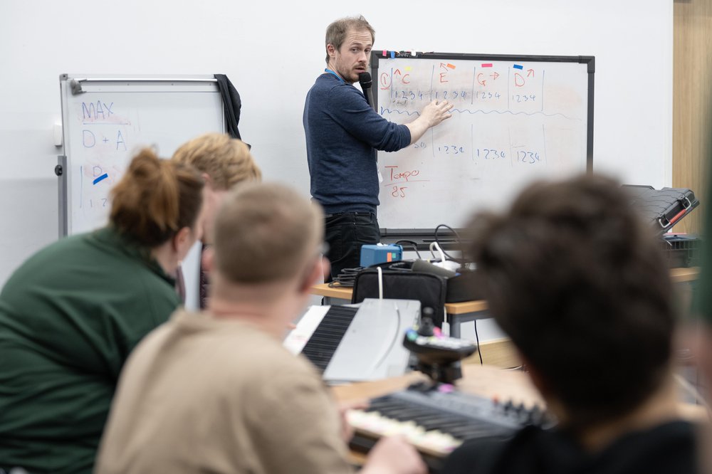 A man wearing a blue jumper teaching 3 young people using a whiteboard.