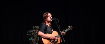 A young girl performing on stage with an acoustic guitar.