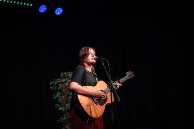 A young girl performing on stage with an acoustic guitar.