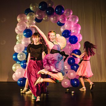 A young dancer jumping in the air in front of a balloon archway