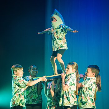 Five young dancers lifting a dancer wearing a shark hat