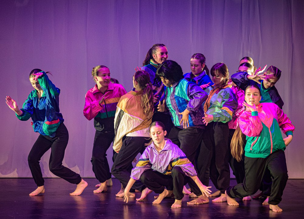 A group of dancers performing on stage wearing brightly coloured jackets