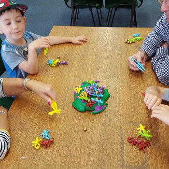 An older man and an older lady play a board game featuring colourful plastic lizards with two boys, aged between 6 and 8.