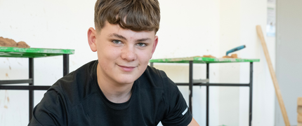 A construction student smiles at the camera whilst checking that a brick wall is level