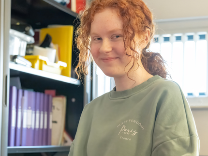 A teenage girl with curly ginger hair in a low pony tail and wearing a sage green jumper smiling.