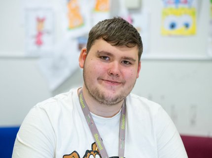 A photo of a young student with short hair. He's smiling while he works on a laptop