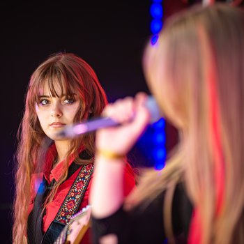 Two girls singing on stage, one is looking at the other