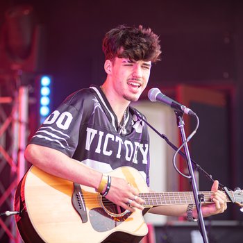A boy in a black shirt singing and playing acoustic guitar on stage
