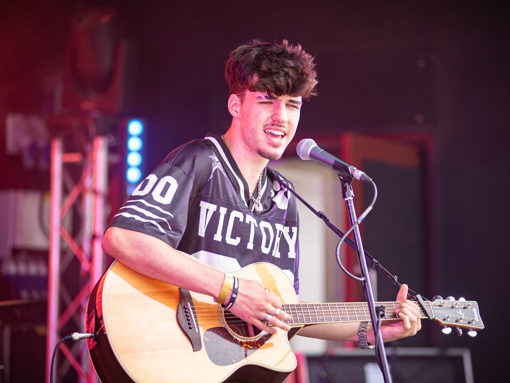 A boy in a black shirt singing and playing acoustic guitar on stage
