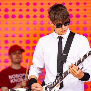 A boy playing guitar wearing sunglasses, a shirt and tie