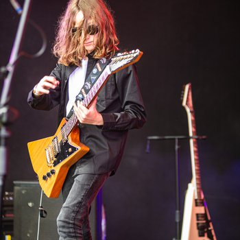 A young person with long hair playing the electric guitar