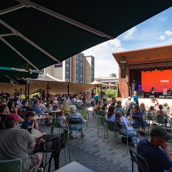 A crowd of people in an outdoor bar watching a stage