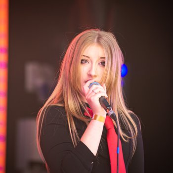 A girl singing wearing a black shirt and red tie