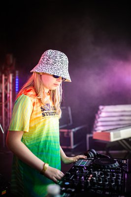 A young person in a colourful t shirt behind DJ decks