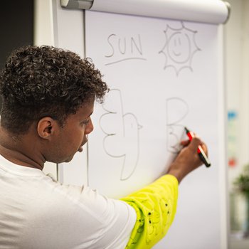 Author RAMZEE draws a cartoon on a whiteboard