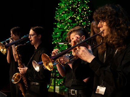 Three musicians playing the trumpet with a christmas tree behind them