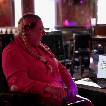 A girl with plaited hair and a pink top sat at a laptop