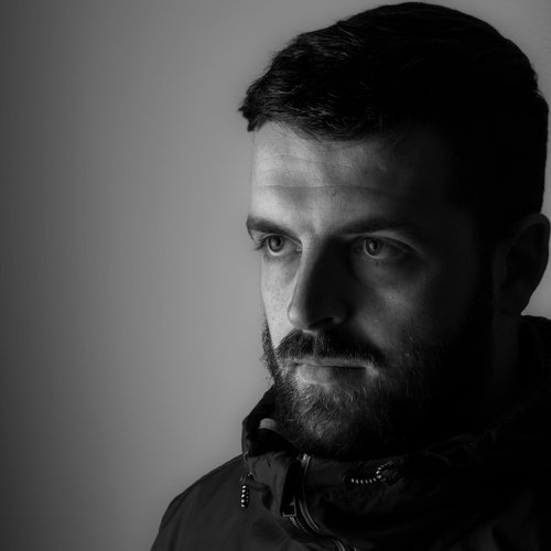 A black and white headshot image of a man wearing a coat.