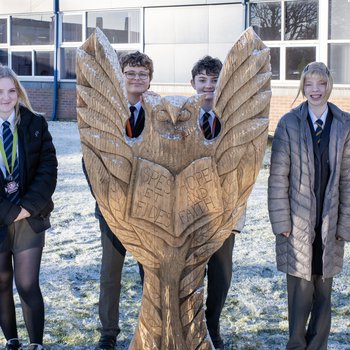 A group of school children stand with a wooden owl sculpture