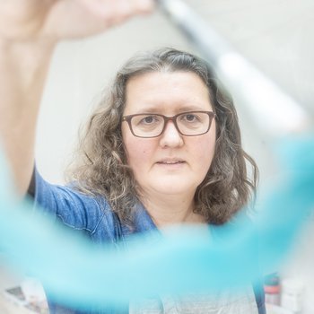 Joy is holding a brush and painting a blue semi circle of paint on what seems to be the photographers camera lense.