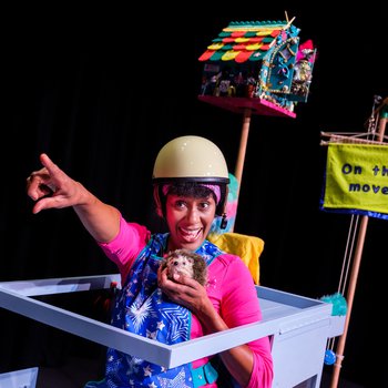 Mavis Sparkle smiling holding mop, stands in front of backdrop of cleaning items