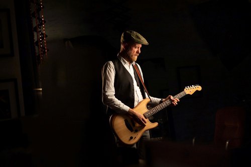 A man playing an acoustic guitar wearing a green flat cap.