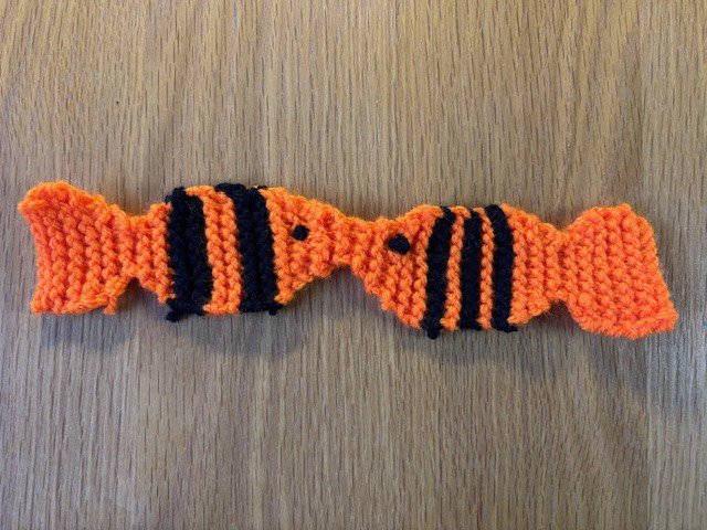 A flat knitted bookmark shaped like two kissing fish