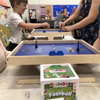 An image of two boards for the game Klask, with the hands and torsos of four players.