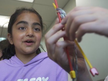 A girl watches someone knit with interest
