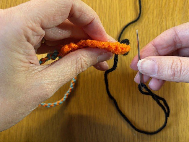 A threaded sewing needle, pulling a piece of yarn through a knitting project