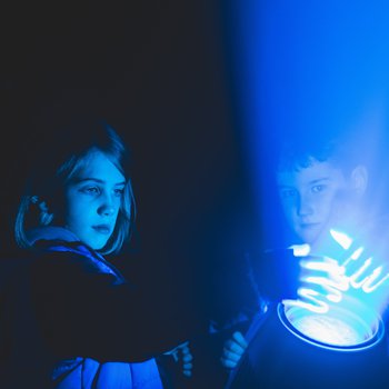 Children holding their hands out in front of a blue light projection.