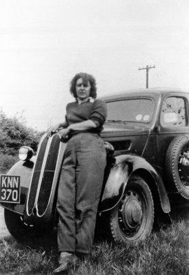 Land Army girl leaning against a car on a farm in Collingham c. 1944