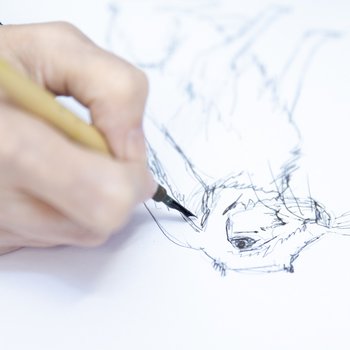 Close up photograph of the artists hand drawing a rabbit with an ink pen