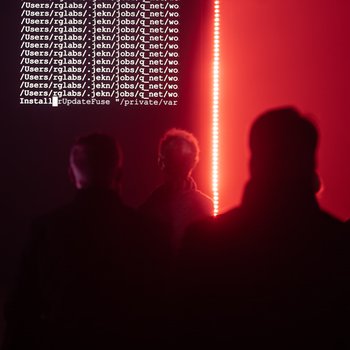 Crowds in a dark church in front of a large screen with red lighting.