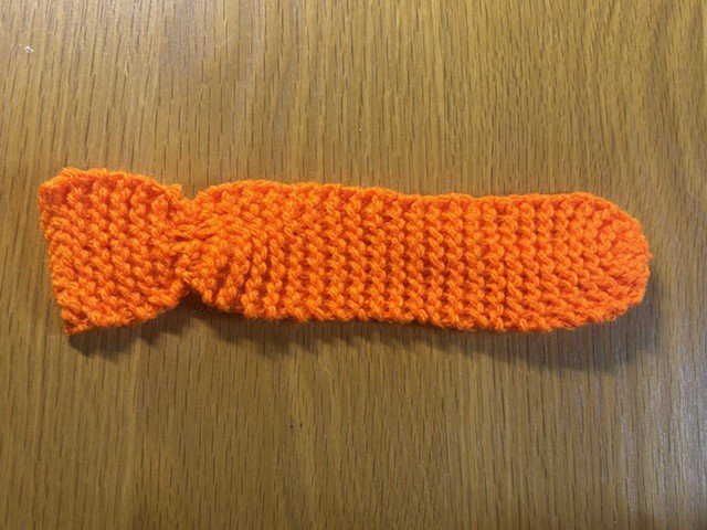 A piece of knitting with gathered sections to give it a rounded end and a fish tail