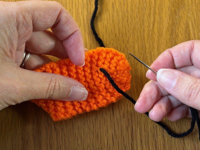 A sewing needle pulling a piece of yarn through a knitting project