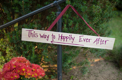 Handwritten sign set against greenery reading: "This way to Happily Ever After"