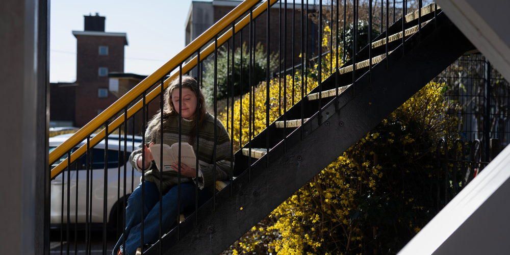 A girl sat on a stairway outside reading a book