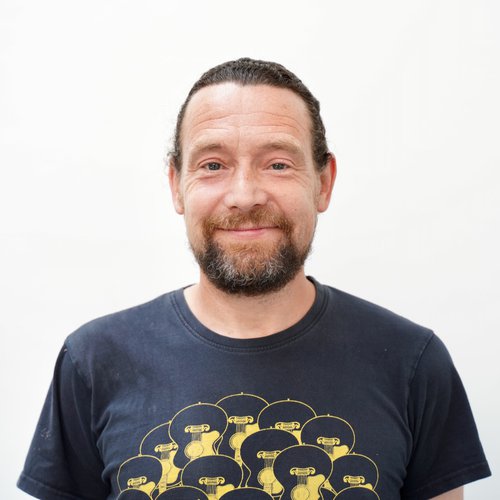 A headshot of a man with brown hair and a beard smiling at the camera.