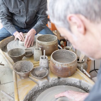 Mark sat at his potters wheel throwing a pot with a mirror in front showing his reflection