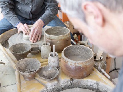 Mark sat at his potters wheel throwing a pot with a mirror in front showing his reflection