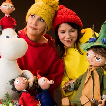 Two people wearing a red and yellow top holding a moomin puppet.