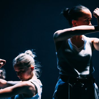 Two female dancers on stage wearing white vests crossing their arms