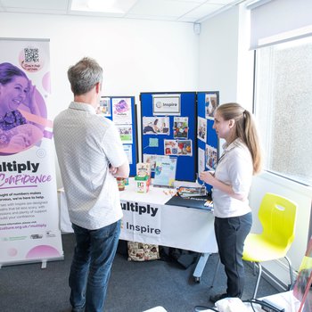 Man and woman talking in front of a promotional stand with a table and pop-up banner with a Multiply graphic