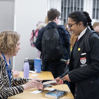 An author wearing a blue shirt stands in an isle of books and holds two copies of his book