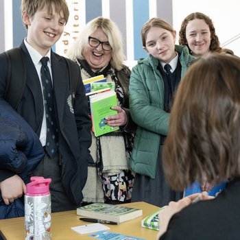 An author wearing a grey shirt stands in an isle of books and holds a copy of his book