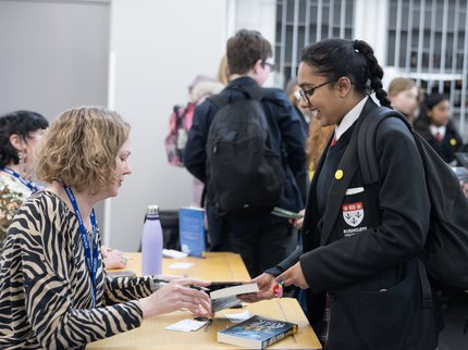 A student holds a book and talks to an author signing her book on a table