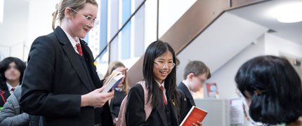 two students stand into front of a woman sitting signing their books